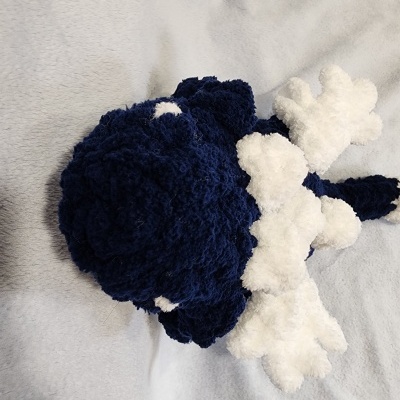 Boneco de pelúcia azul e branco sobre tecido cinza