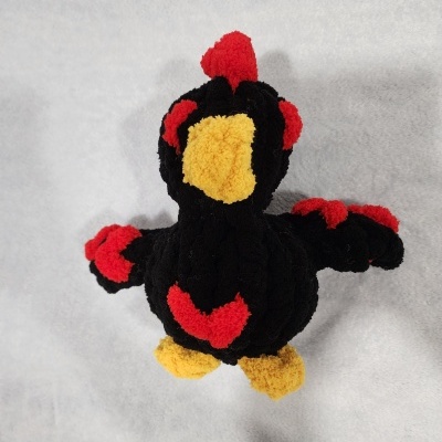 Peluche pássaro negro com detalhes vermelhos e amarelos visto de cima