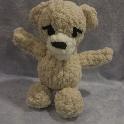 Urso de peluche bege com olhos e nariz pretos sobre fundo cinzento