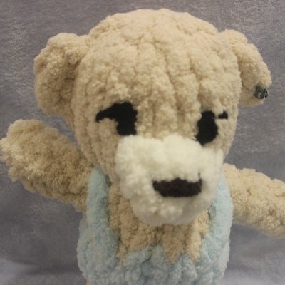 Ursinho de peluche bege com colete azul claro e fundo cinzento