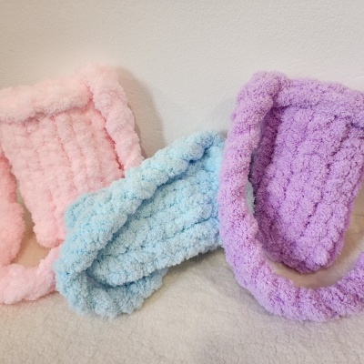 Três malas de pelúcia coloridas em rosa, azul e lilás com textura felpuda