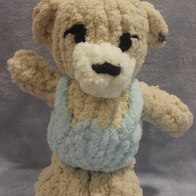 Ursinho de peluche bege com vestido azul claro em fundo cinzento