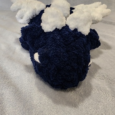 Brinquedo de pelúcia azul com chifres brancos sobre tecido cinzento