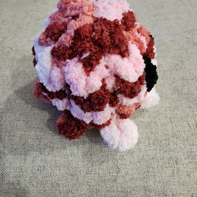 Boneco de pelúcia feito com pompons de lã coloridos sobre sofá cinza.
