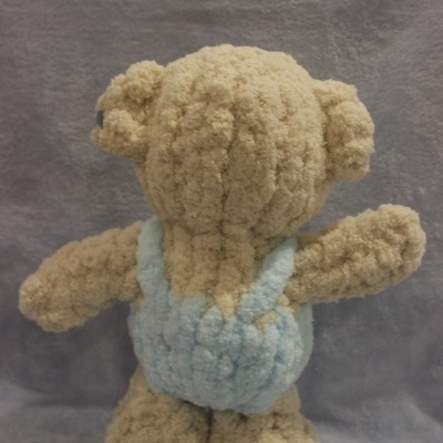 Urso de peluche bege com fato azul claro sobre fundo cinzento