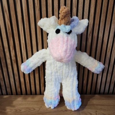 Pelúcia de unicórnio felpudo colorido em fundo de madeira com riscas verticais.