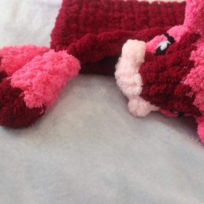 Peluche felpudo rosa, vermelho e branco sobre uma superfície cinzenta