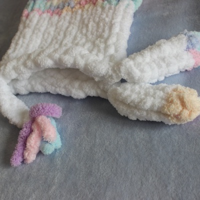 Cachecol branco fofo com pontas coloridas numa superfície cinzenta