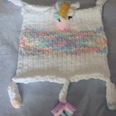 Manta ou cobertor em crochet branca com faixas pastel e unicórnio em relevo.
