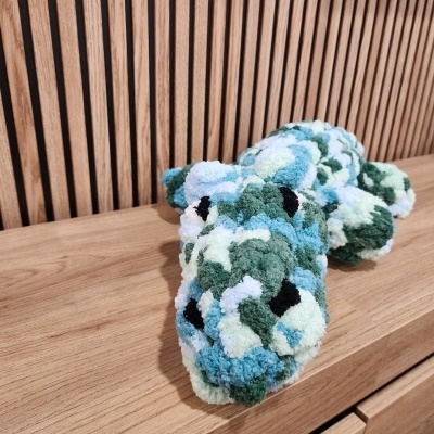 Pelúcia em forma de crocodilo com padrão azul, verde, branco e preto sobre superfície de madeira