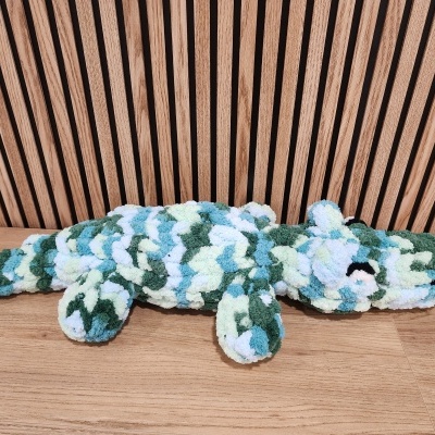 Brinquedo peluche crocodilo multicor sobre madeira clara e fundo ripado de madeira