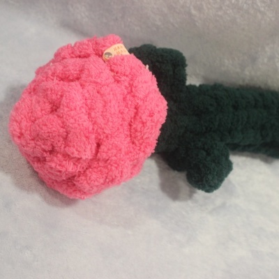 Flor artesanal em lã rosa com caule verde escuro sobre fundo cinza