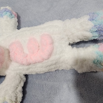 Pelúcia branca macia com detalhes coloridos nas patas e orelhas sobre superfície azul clara