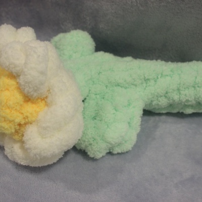 Flor decorativa felpuda com pétalas brancas, centro amarelo e folhas verdes