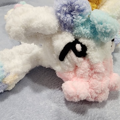 Peluches de unicórnios felpudos coloridos com olhos bordados sobre tecido cinzento