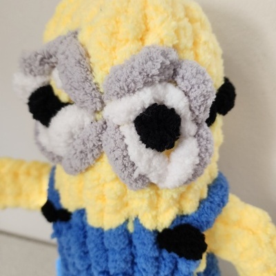 Boneco Minion amarelo de tecido felpudo com olhos cinzentos e roupa azul.