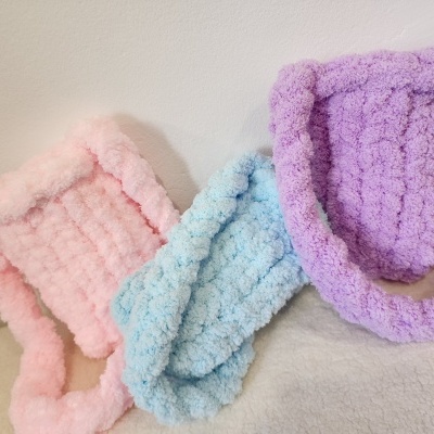Três faixas de cabelo felpudas rosa, azul e lilás sobre superfície branca.
