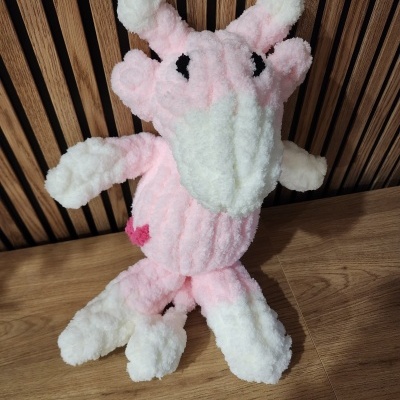 Pelúcia fofinha rosa e branca sentada em chão de madeira com fundo de ripas de madeira