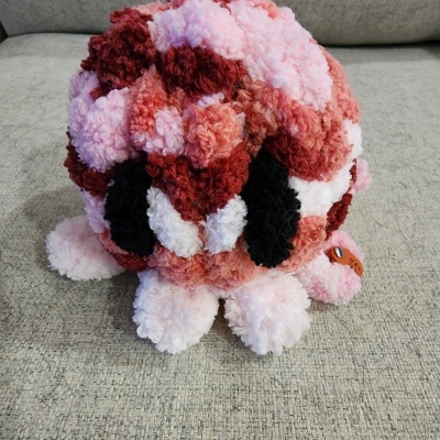 Pelúcia artesanal felpuda cor-de-rosa, vermelho, branco e preto com etiqueta de couro num sofá cinzento