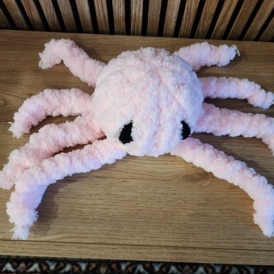 Brinquedo macio rosa em forma de polvo com olhos pretos sobre madeira