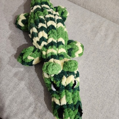 Pelúcia de crocodilo verde e amarelo claro sobre sofá cinzento