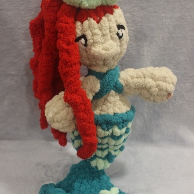 Boneca de tricot sereia com cabelo vermelho e cauda azul em fundo cinzento