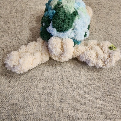 Brinquedo de pelúcia texturizado verde, azul e bege sobre tecido bege