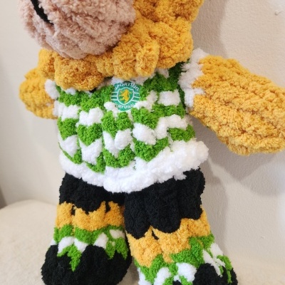 Boneco de peluche amarelo e bege com camiseta verde e branca e pernas com padrões coloridos