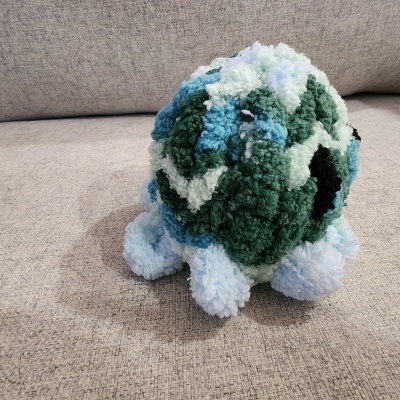 Boneco de pelúcia colorido feito em pompons sobre sofá cinzento