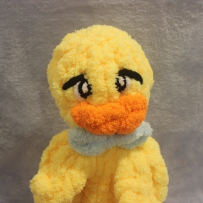 Pelúcia de pato amarelo com bico e olhos expressivos e gravata azul clara