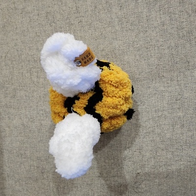 Dois scrunchies felpudos, um branco com etiqueta HAND MADE e outro amarelo com riscas pretas, sobre fundo cinzento