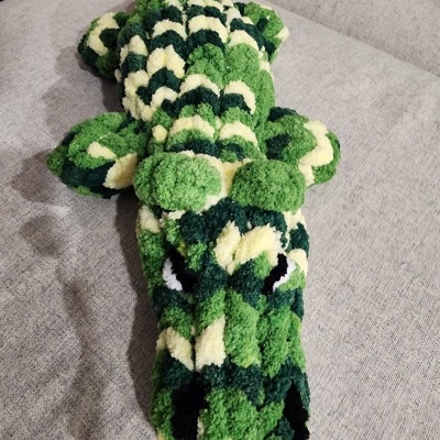 almofada felpuda em forma de crocodilo verde e branco numa superfície cinza