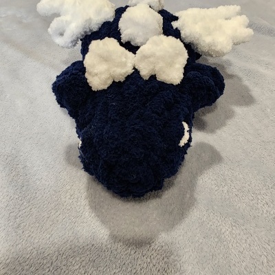 Pelúcia ou almofada azul escuro com detalhes brancos sobre superfície cinza.