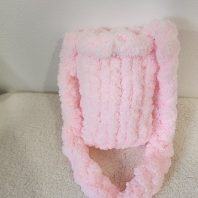 Bolsa de mão felpuda cor-de-rosa com alças do mesmo material sobre superfície bege