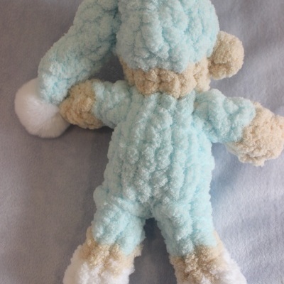 Boneco de pelúcia azul claro e bege com gorro pontudo e pompom branco visto de costas