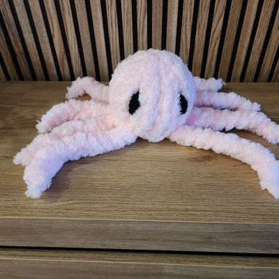 Pelúcia rosa em forma de polvo com olhos pretos sobre madeira clara