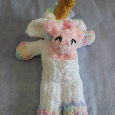 Pelúcia de unicórnio com corpo branco e detalhes coloridos sobre superfície cinzenta