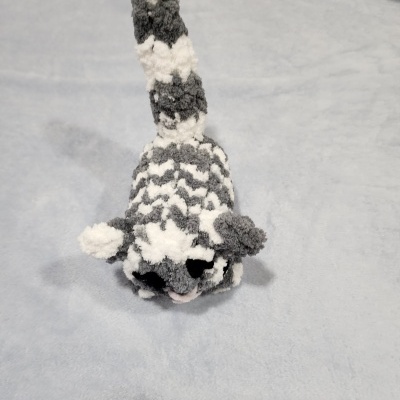 Pelúcia de gato cinzenta e branca com pelos ondulados sobre tecido cinzento claro