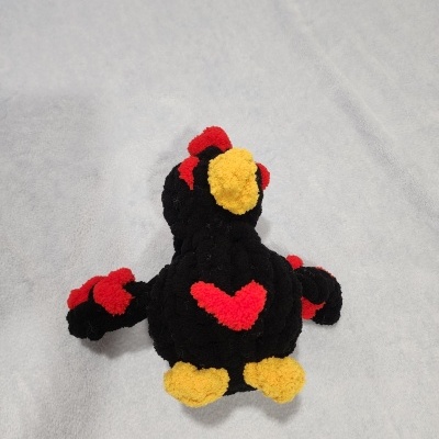 Pelúcia preta com detalhes vermelhos e amarelos sobre tecido cinzento claro