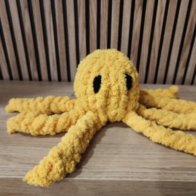 Boneco amarelo de polvo felpudo com olhos pretos em superfície de madeira