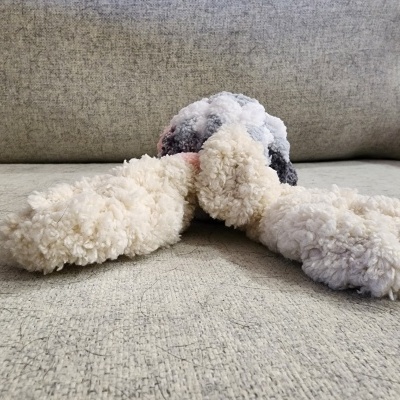 Cachorro de pelúcia colorido com textura felpuda deitado num sofá cinza
