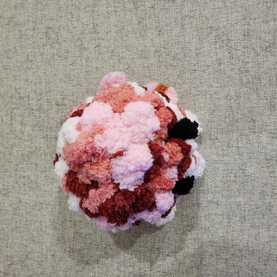 Objeto artesanal de pompons de lã coloridos sobre superfície cinza