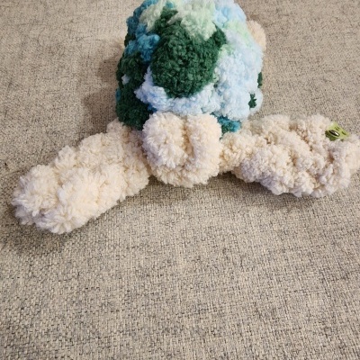 Brinquedo peluche tartaruga verde azul e creme sobre tecido bege