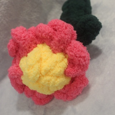 Flor de pelúcia amarela e vermelha com caule verde escuro sobre fundo claro