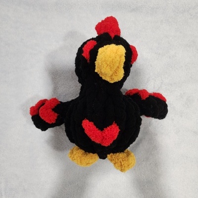 Pelúcia de pássaro preto, amarelo e vermelho sobre superfície cinza clara