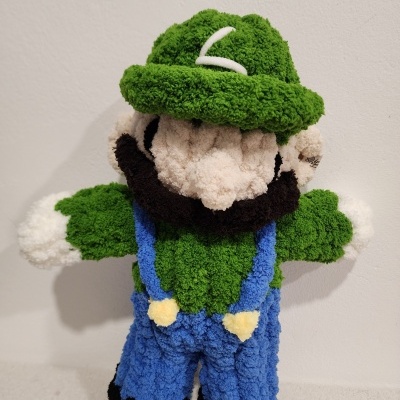 Boneco peluche verde com chapéu e fato azul sobre fundo branco