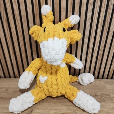 Pelúcia amarela e branca de girafa em malha sentada sobre madeira com fundo de painéis de madeira