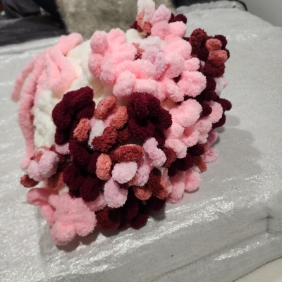 Produto artesanal de crochê com pompons coloridos sobre superfície prateada