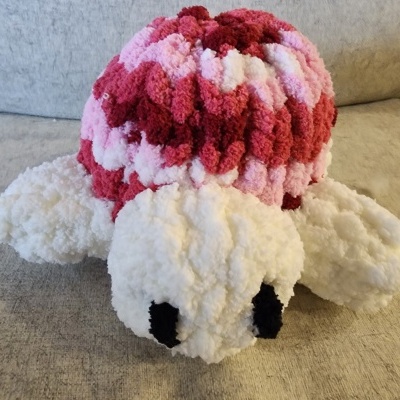 Pelúcia de tartaruga felpuda em cores vermelha, rosa, branca e preta numa almofada cinza