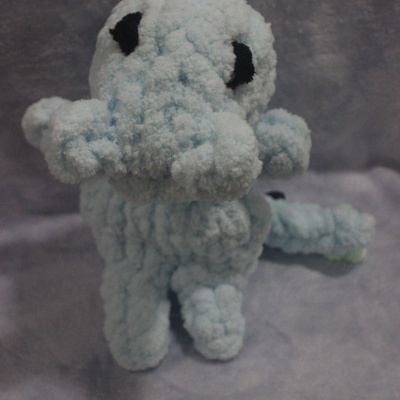 Pelúcia azul clara com olhos pretos e pompom azul escuro, textura felpuda, fundo cinza